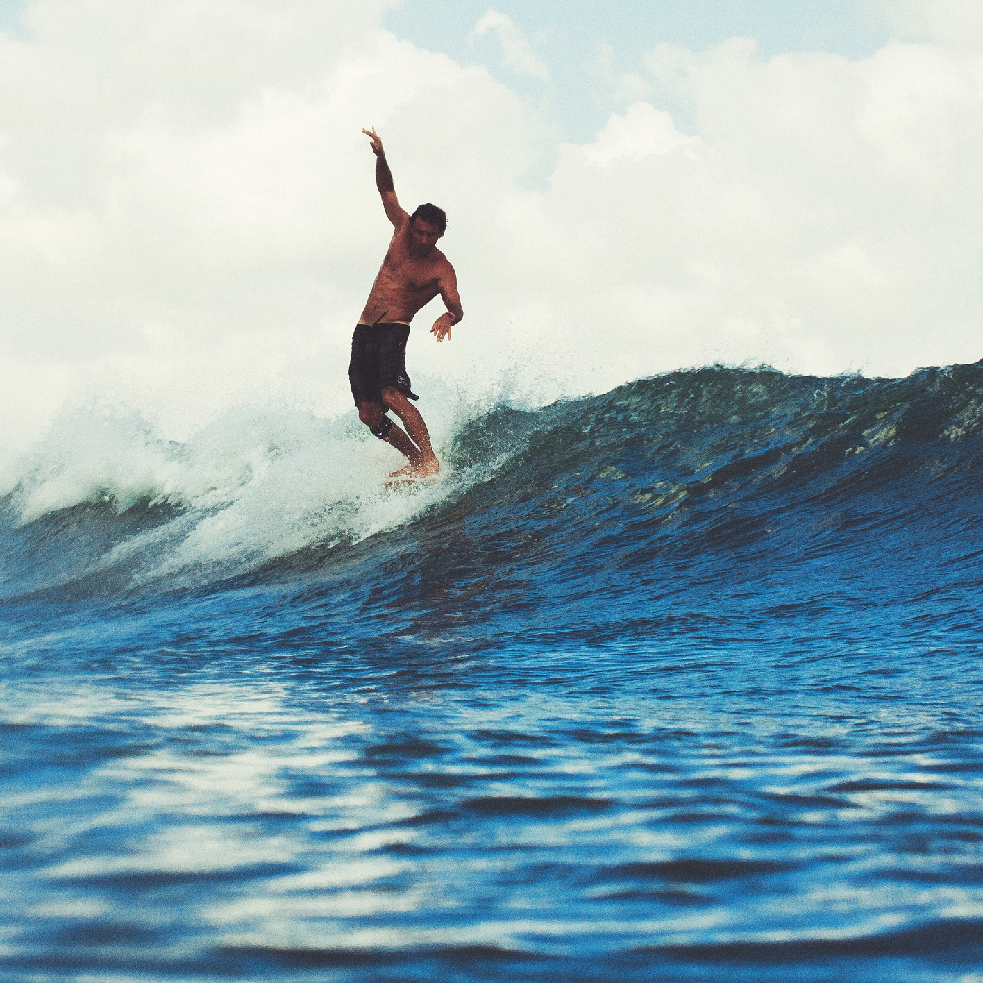 a male surfer riding a wave topless