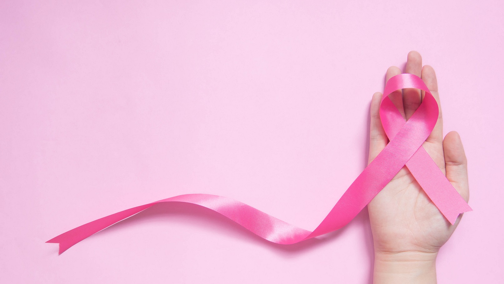 hand holding ribbon in the shape of breast cancer symbol