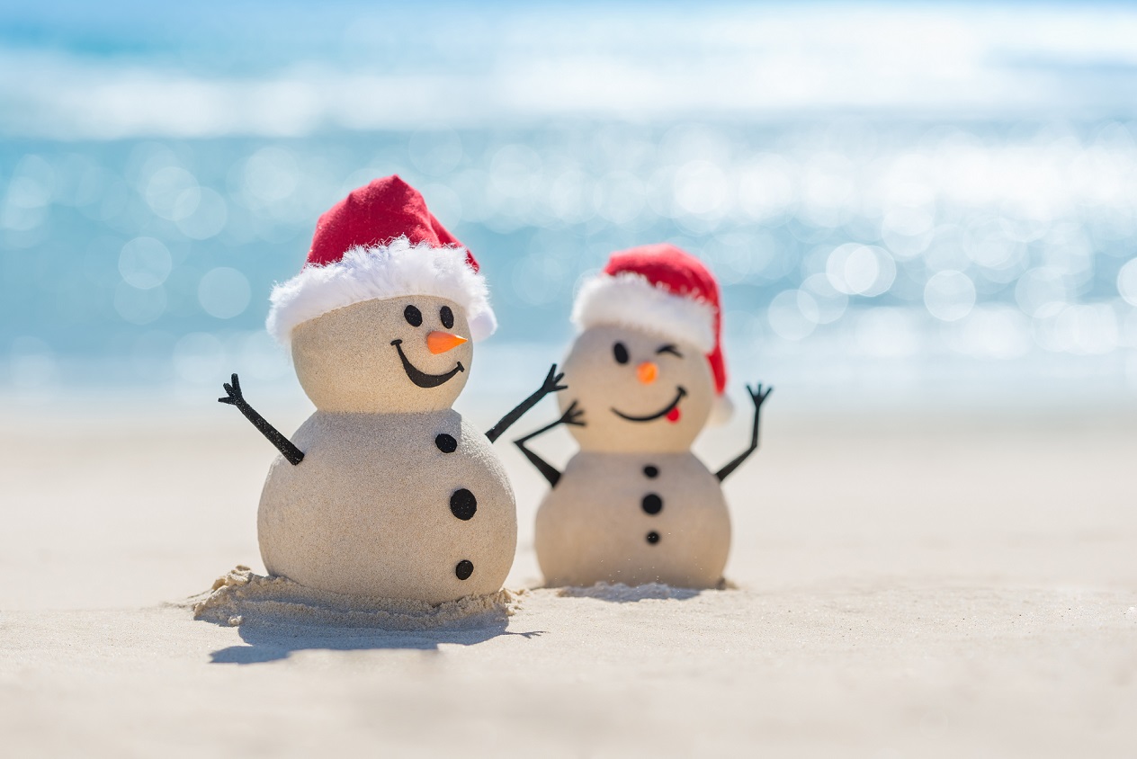 two snow men made out of sand on the beach with santa hats