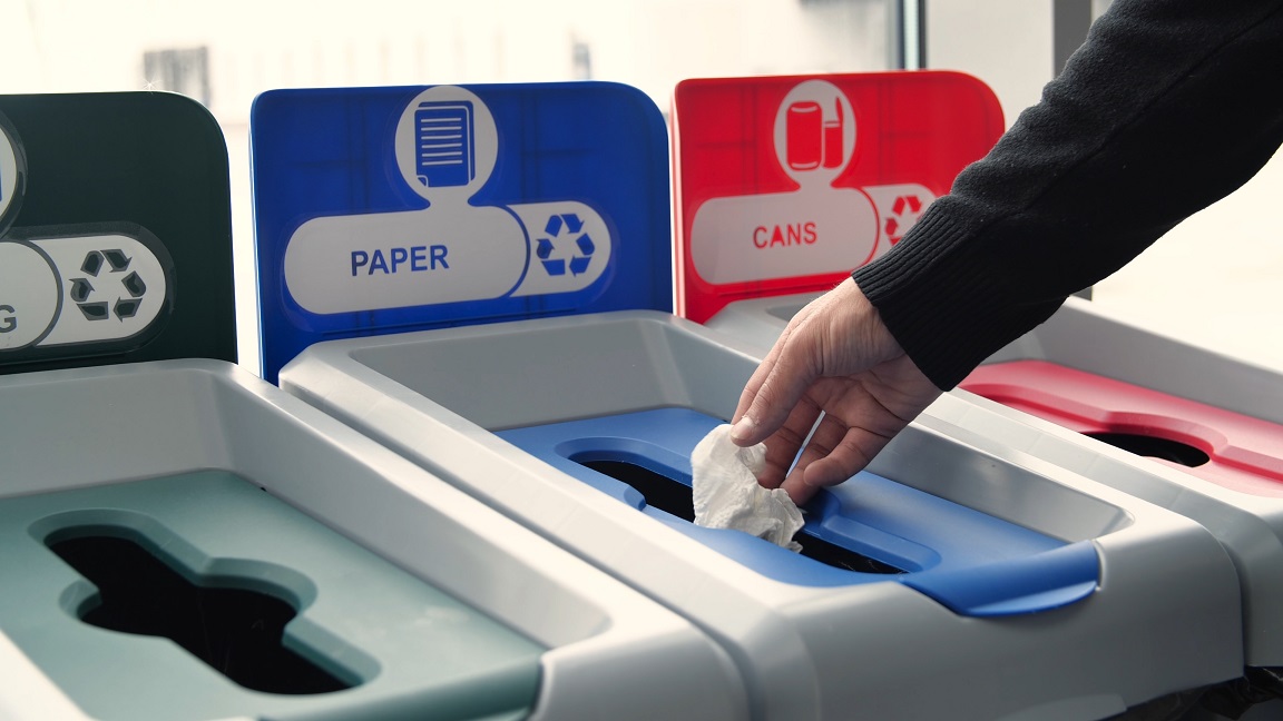 a hand recycling paper into the proper trash can for paper recycling